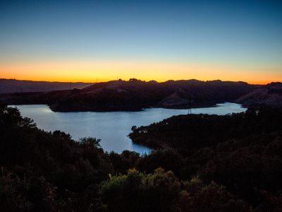 an overhead view of the briones reservoir at sunset. the water appears also silver in the blue and orange light of the evening